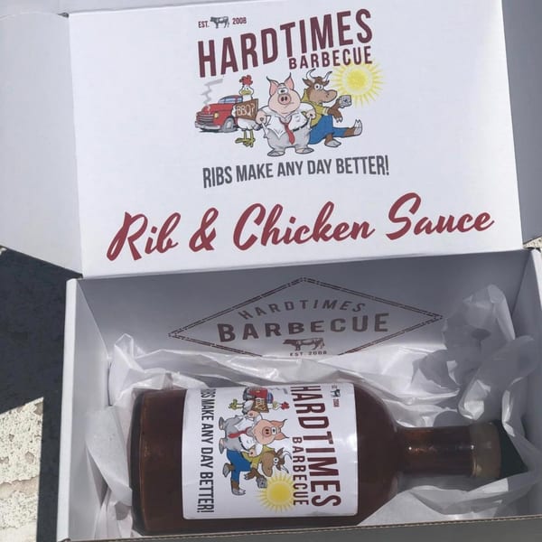 Hard Times BBQ sauce bottle in a white box with the brand's cartoon logo on the label.