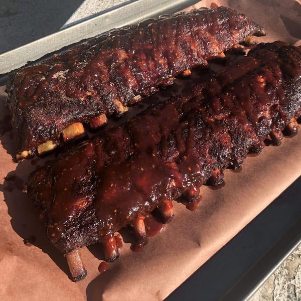 Two racks of Hard Times BBQ ribs, glistening with dark barbecue sauce, on brown paper.