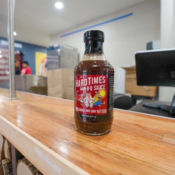 A bottle of Hard Times Bar-B-Q Sauce with a red label sits on a wooden counter.