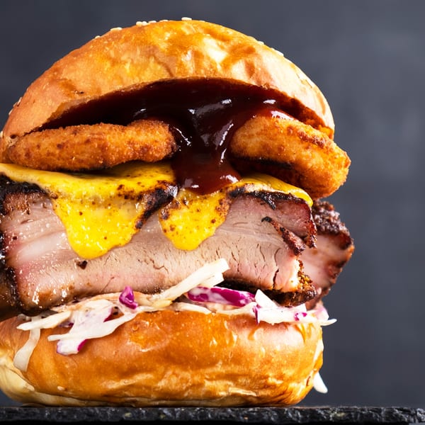 Hard Times BBQ sandwich with thick-cut brisket, melted cheese, onion rings, coleslaw, and barbecue sauce.
