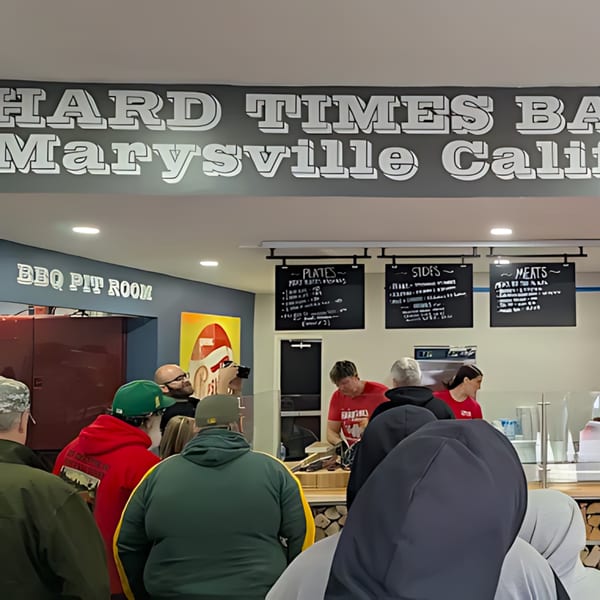 Customers line up at Hard Times BBQ, with staff serving food behind a counter.