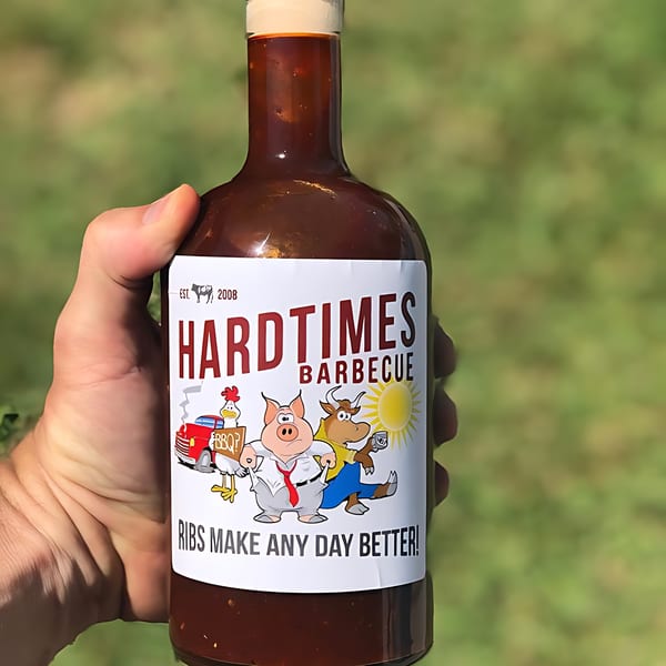 A hand holds a bottle of Hard Times Barbecue sauce with a cartoon pig, cow, and chicken on the label.