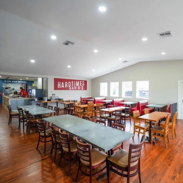 Spacious Hard Times BBQ dining room with long tables, red booths, and a service counter.