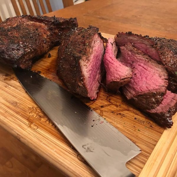 Hard Times BBQ's sliced, medium-rare smoked tri-tip steak on a wooden cutting board with a knife.