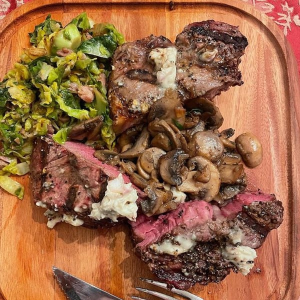 Hard Times BBQ steak with mushrooms and green vegetables on a wooden board.