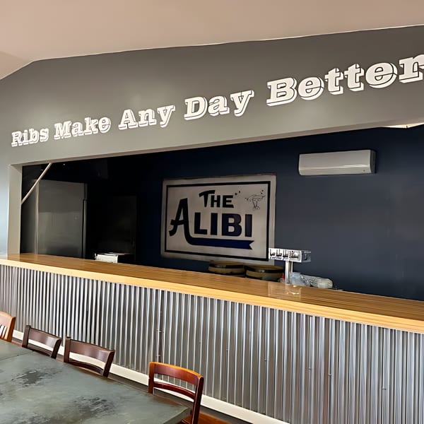 Interior of Hard Times BBQ with a corrugated metal bar, wooden top, and "The Alibi" sign.