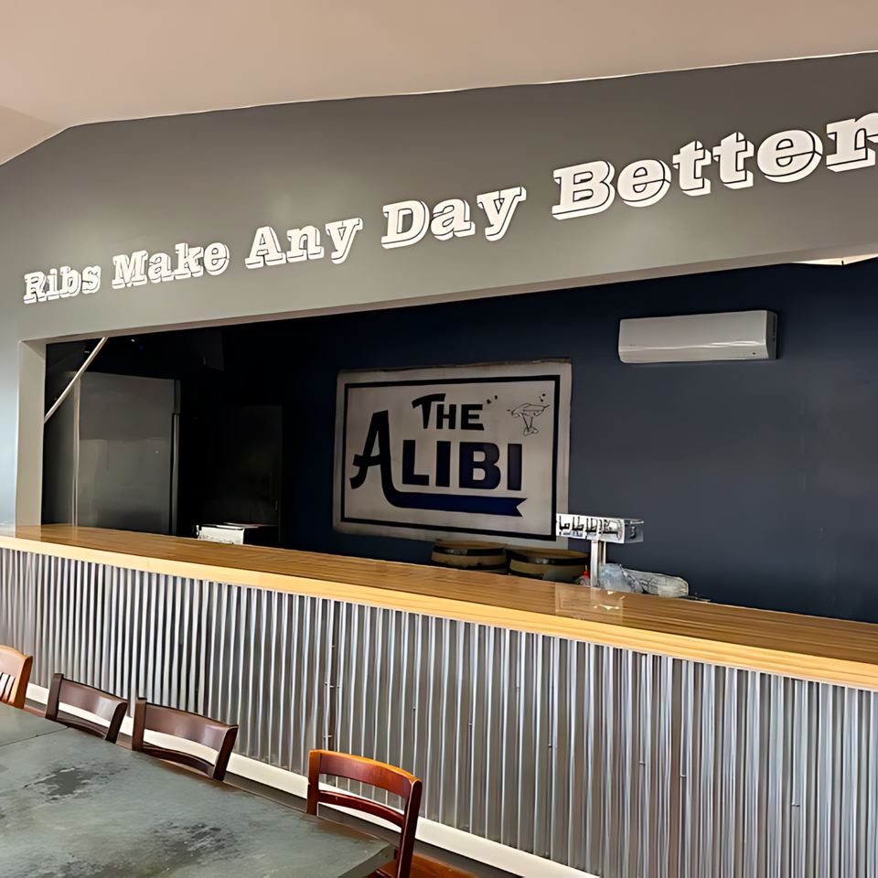 Interior of Hard Times BBQ with a corrugated metal bar, wooden top, and "The Alibi" sign.